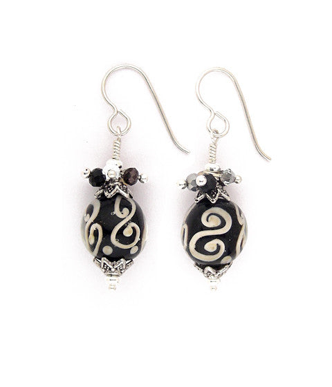 Layers of glass create these eye catching beads, Black with cream colored swirls form the core with clear, smooth glass over that. Topped with pewter caps and a subtle, sweet collection of crystals in jet, silver, smoke and opal. Hand wrapped. A touch over 1.5” long