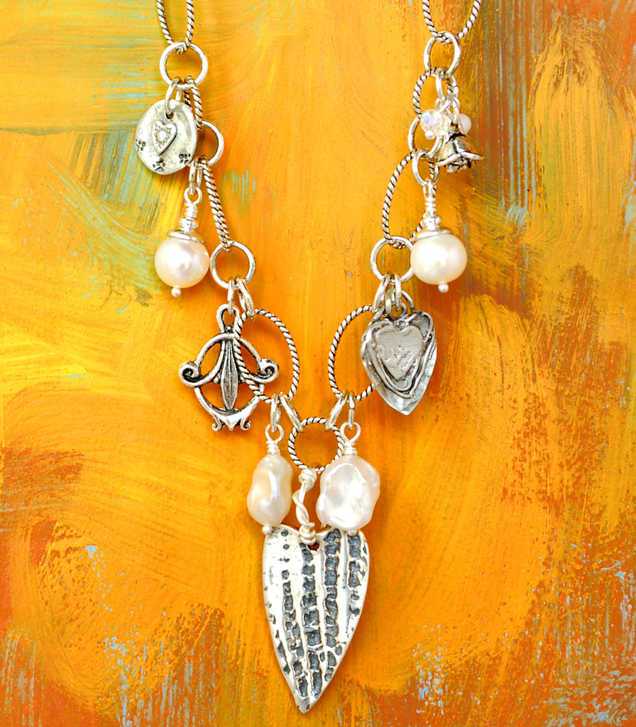 A signature Desert Heart design.  Deb's original pewter hearts dangle on some seriously gorgeous sterling plated and antiqued brass chain.  With freshwater pearls, a couple of crystal beads, and rounded out with a couple interesting pewter charms.  Stretches a generous 21" and can be clasped anywhere on the chain.